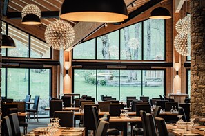 A restaurant interior with high ceilings, large windows, and modern pendant lighting. - Hôtel Club le Crêt (Morzine)