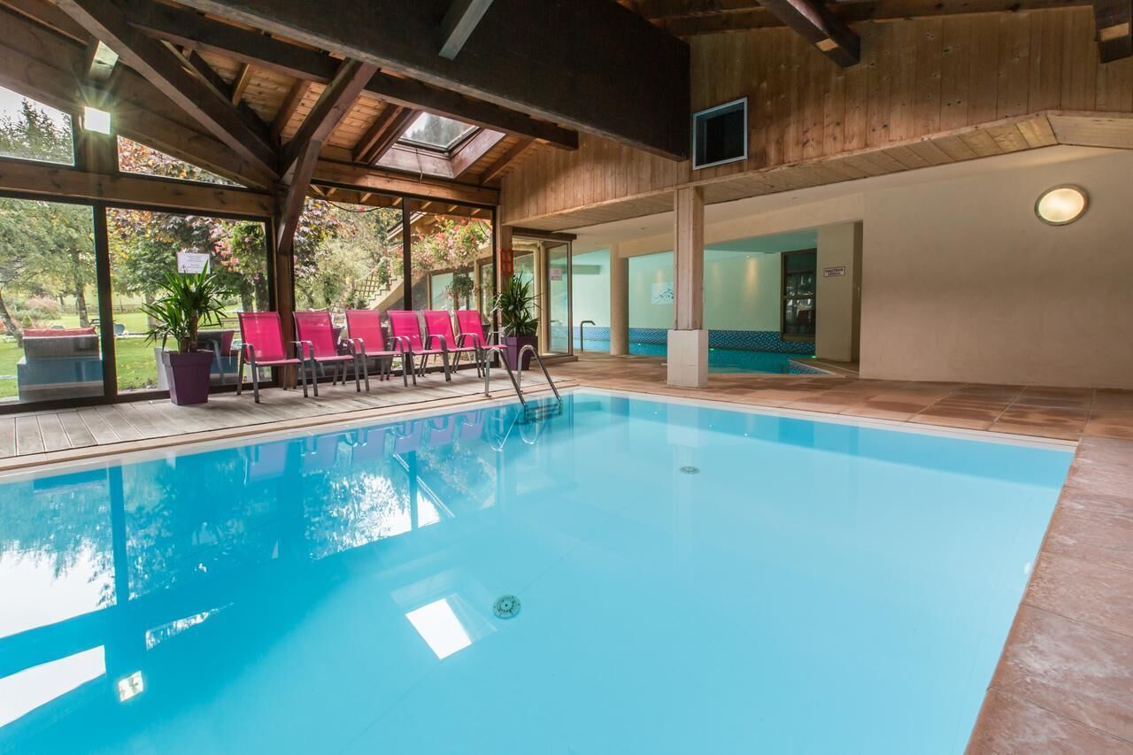 An indoor swimming pool with clear blue water, surrounded by wooden beams and large windows.