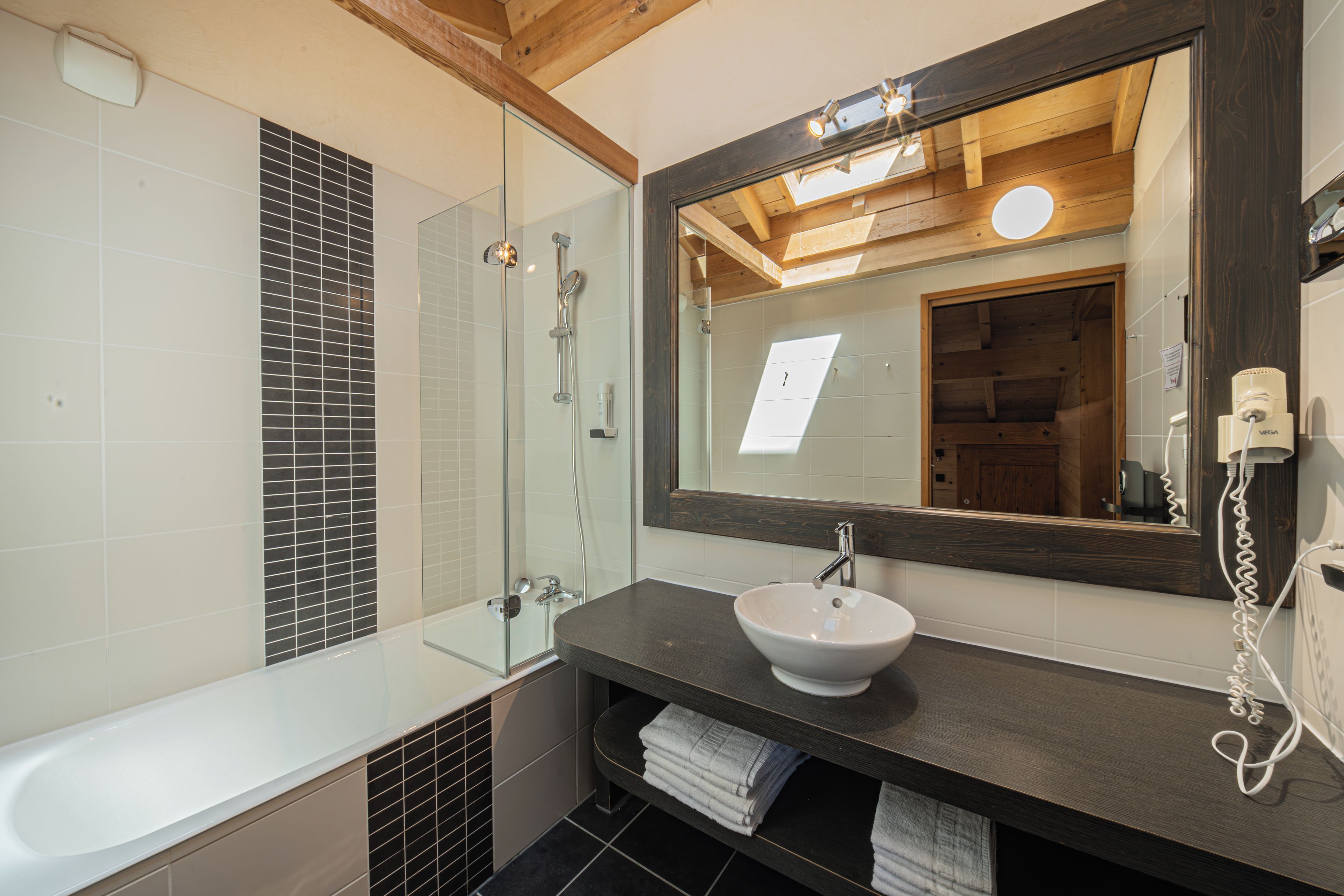 Een badkamer met een witte badkuip, een douche met glazen wanden en een wastafel met spiegel.