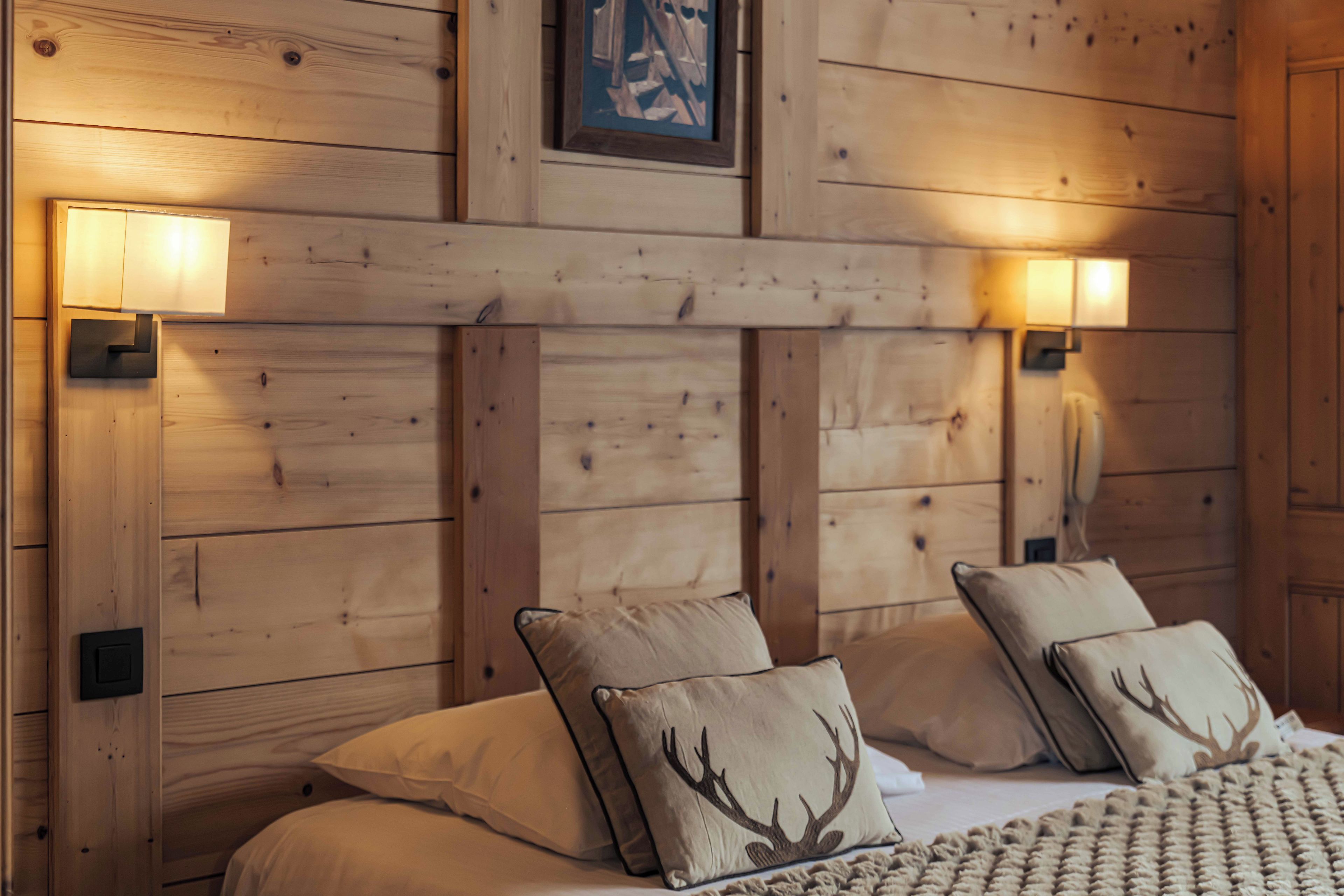 Une pièce en bois avec un lit, deux lampes fixées au mur et un tableau encadré au-dessus du lit.
