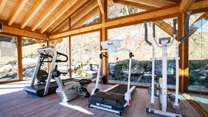 Ein Fitnessstudio mit Laufbändern, Crosstrainern und Kraftgeräten, ausgestattet mit großen Fenstern und Holzbalken.