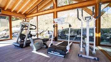 Une salle de sport équipée de tapis de course, de vélos elliptiques et d’appareils de musculation, avec de grandes fenêtres et des poutres en bois.