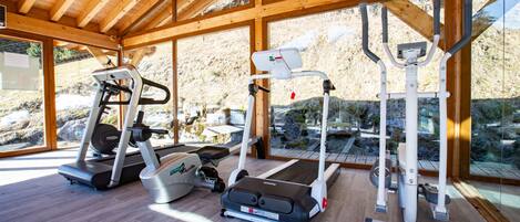 Un gimnasio con cintas de correr, elípticas y máquinas de pesas, que cuenta con amplias ventanas y vigas de madera.