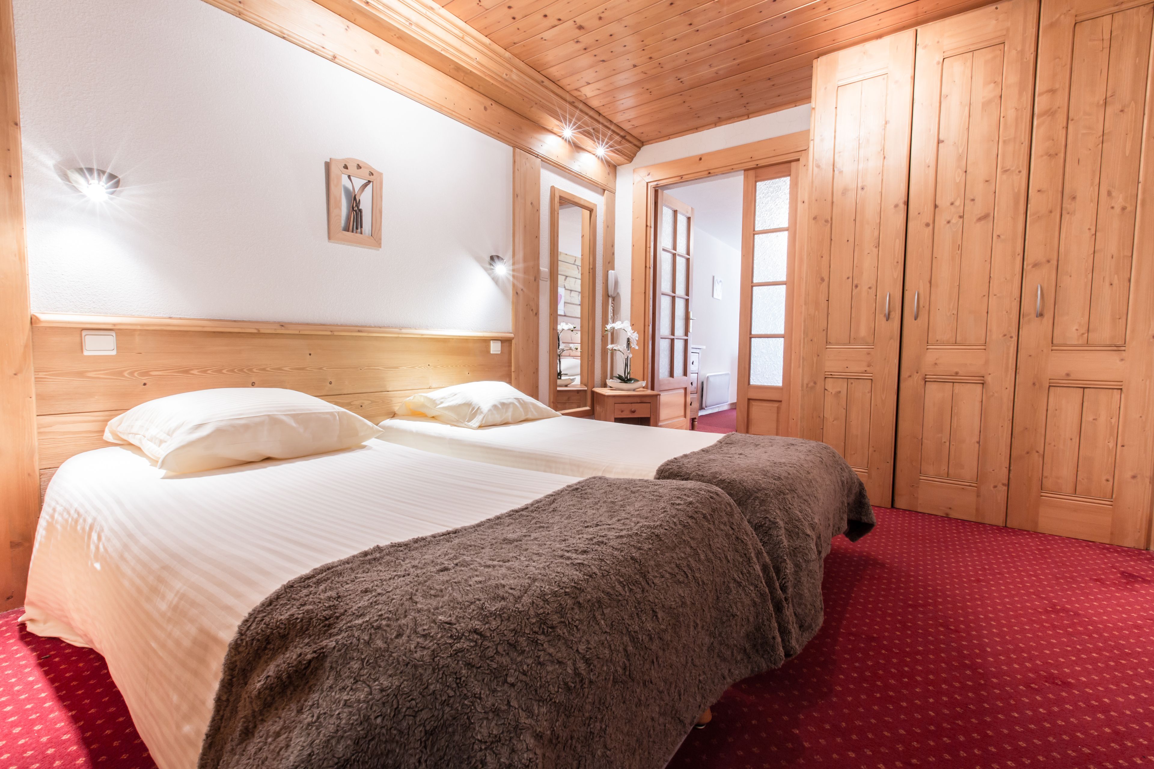 A hotel room with a wooden ceiling, two beds with white linens, a red carpet, and wooden wardrobes.