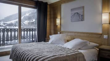 A hotel room with a bed, a nightstand, a painting, and a view of a snowy mountain.
