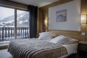 Una habitación de hotel con una cama, una mesita de noche, un cuadro y vistas a una montaña nevada.