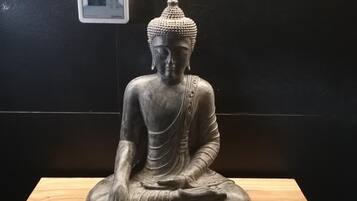 Une statue représentant une figure assise, placée sur une plateforme en bois devant un mur sombre.