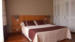 A bedroom with a wooden headboard, a bed with a white and brown bedspread, two bedside tables, and a wardrobe with louvered doors. - La Residence du Rova (Antananarivo)