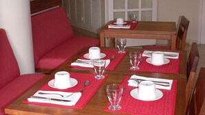 A dining area with a wooden table set for four, red cushioned chairs, and a red mat under each place setting. - La Residence du Rova (Antananarivo)