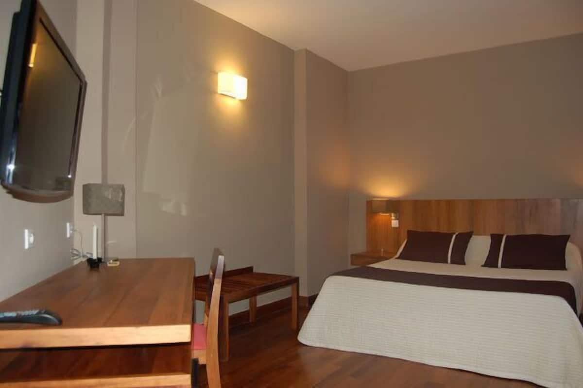 A hotel room with a wooden desk, a bed with a white and brown bedspread, and a wall-mounted TV.