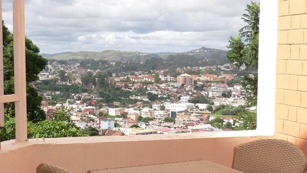 A balcony with wicker furniture overlooking a cityscape. - La Residence du Rova (Antananarivo)