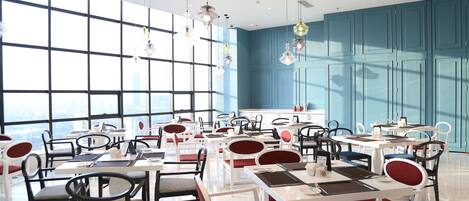 Un comedor moderno con mesas y sillas blancas, ventanas grandes y paredes azules.