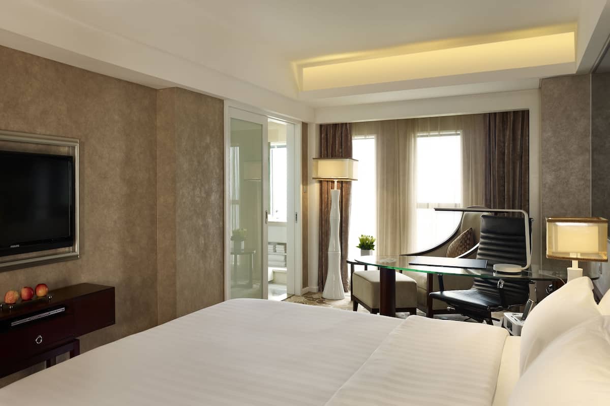 Ein Hotelzimmer mit einem großen Bett, einem Flachbildfernseher, einem Schreibtisch mit Stuhl und einem Glastisch.