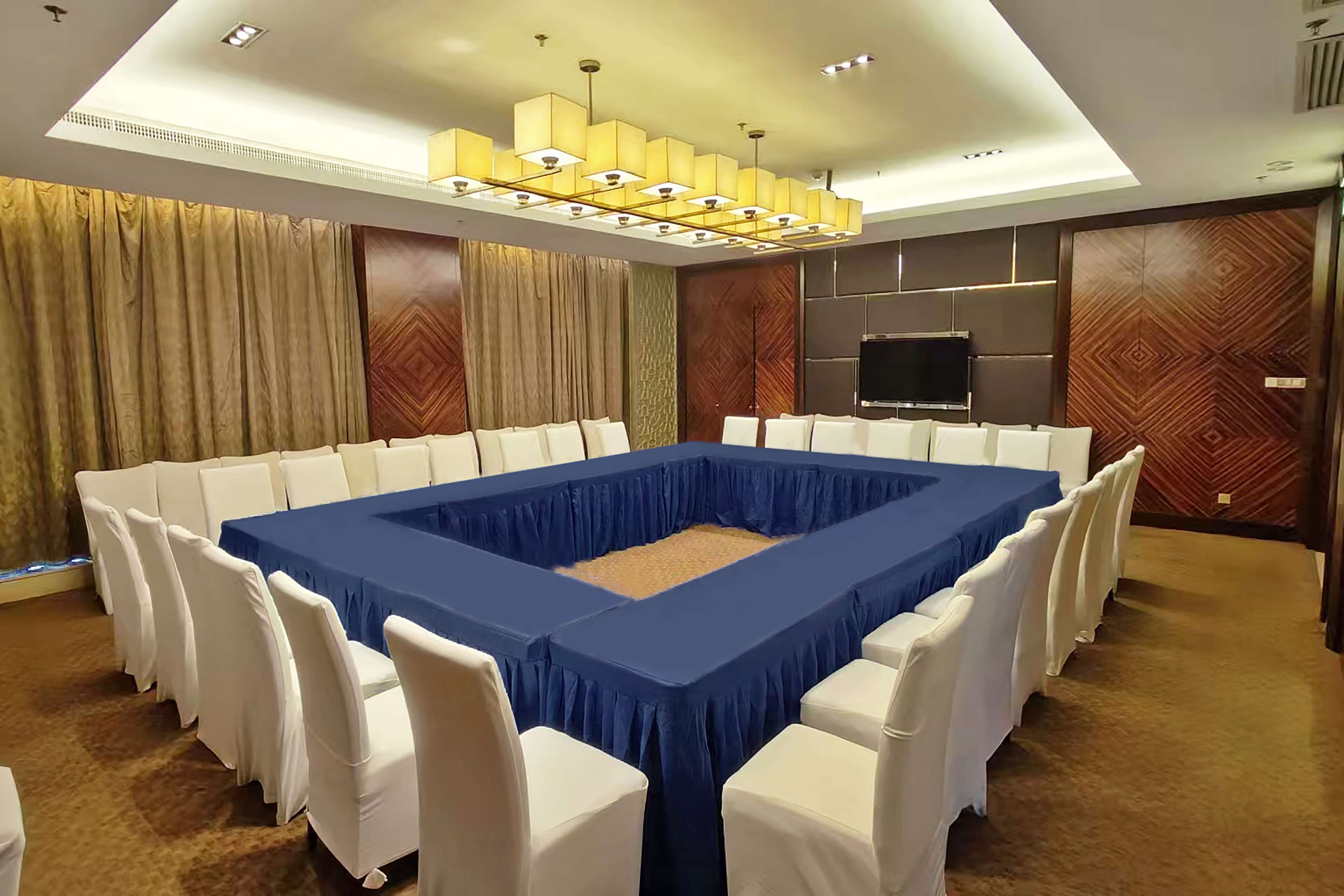 A conference room with a large rectangular table, white chairs, a flat-screen TV, and a modern chandelier.