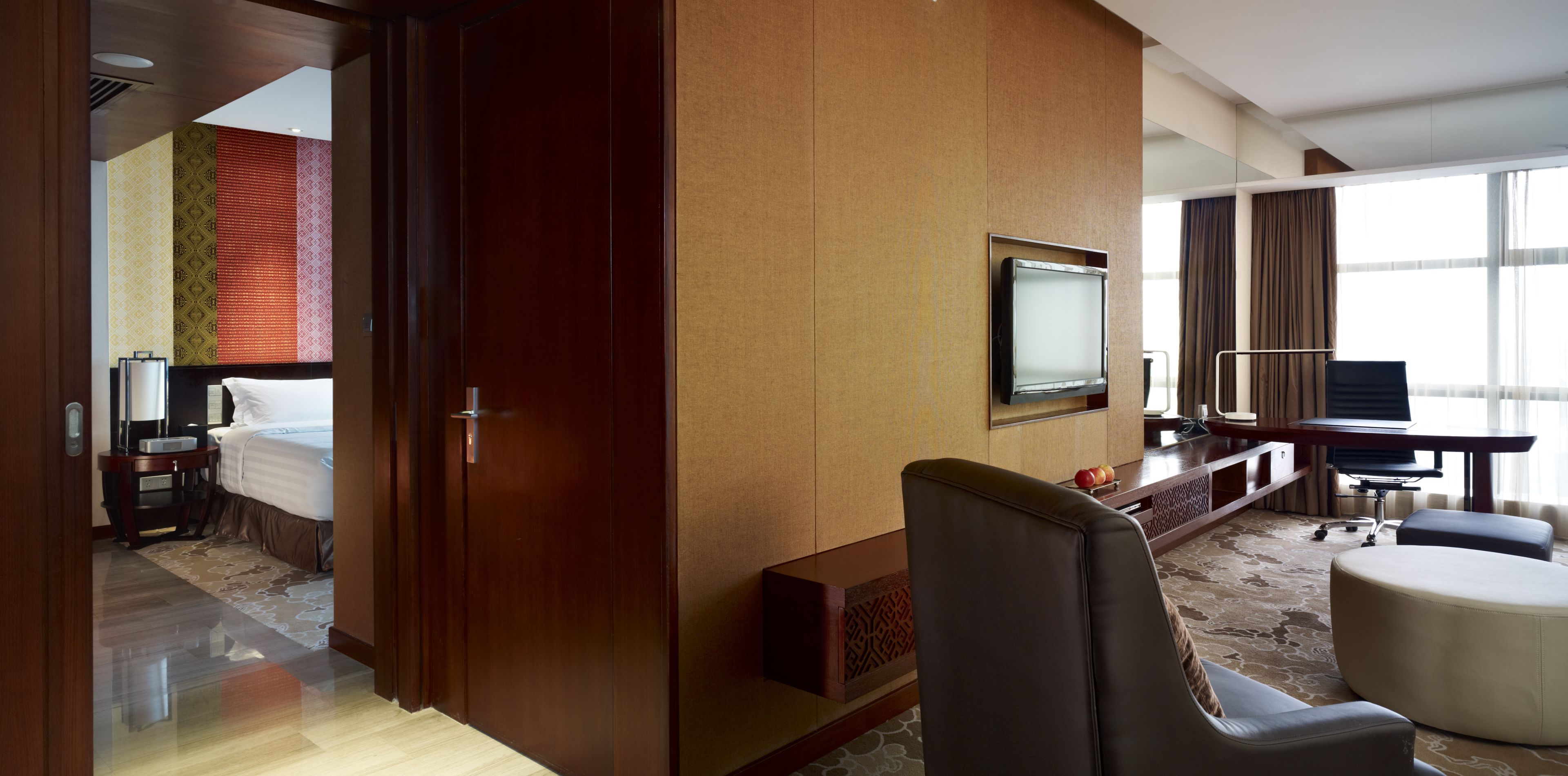 A hotel room with a bed, a desk with a computer, a TV, and a seating area with ottomans.
