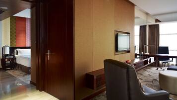 A hotel room with a bed, a desk with a computer, a TV, and a seating area with ottomans.