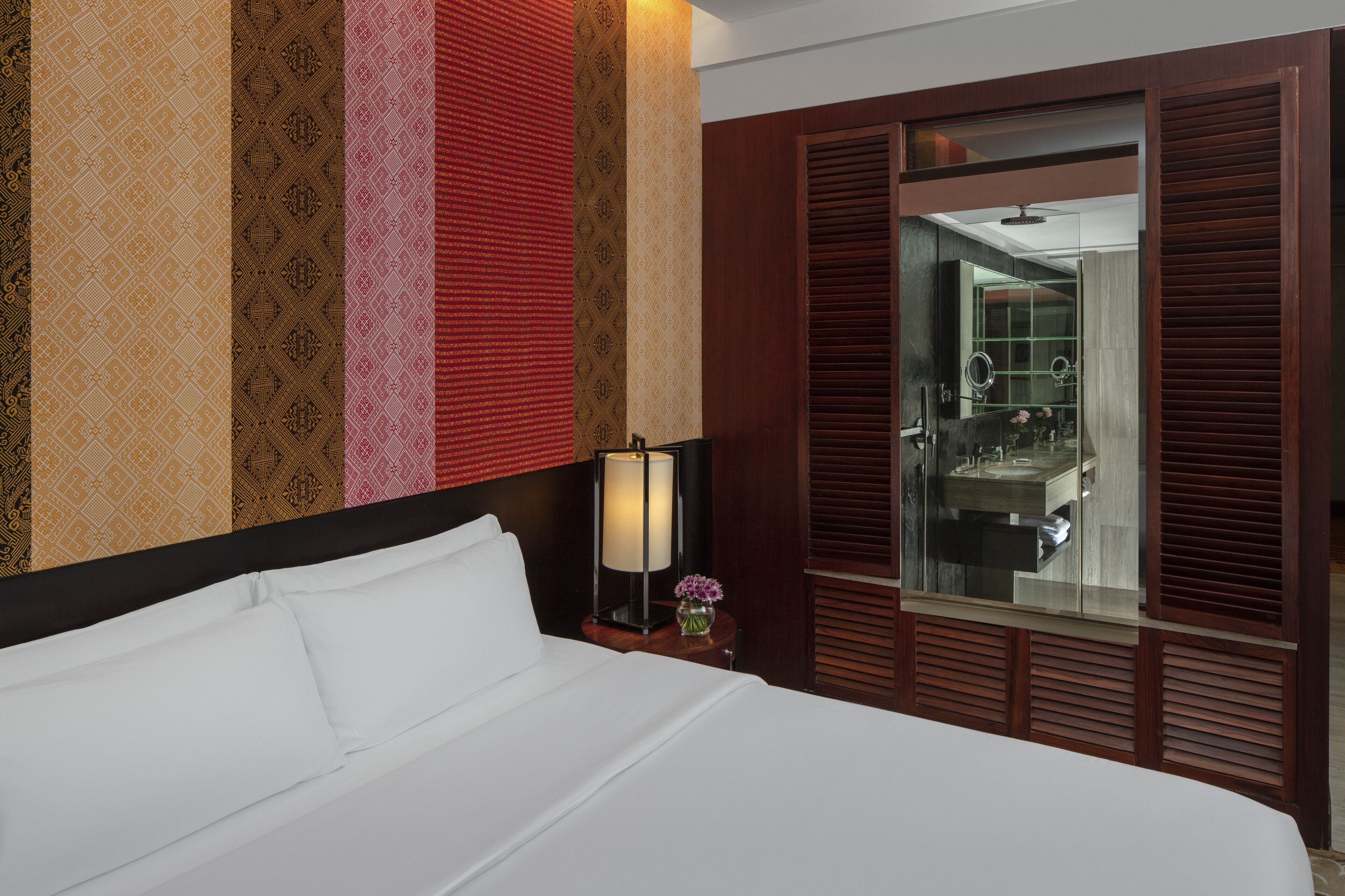 A hotel room with a large bed, a bedside table with a lamp, a mirror, and a wardrobe with a mirror.