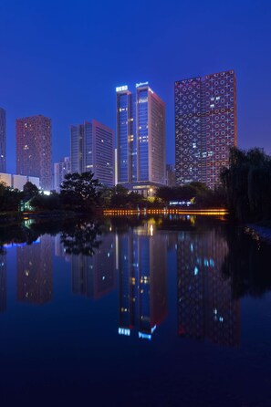 A cityscape at dusk with high-rise buildings reflected in a calm body of water. - Radisson Blu Hotel Liuzhou (Liuzhou)