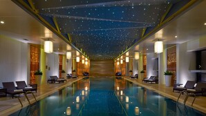 Un hall de hotel con una piscina central, sillones de descanso e iluminación decorativa.