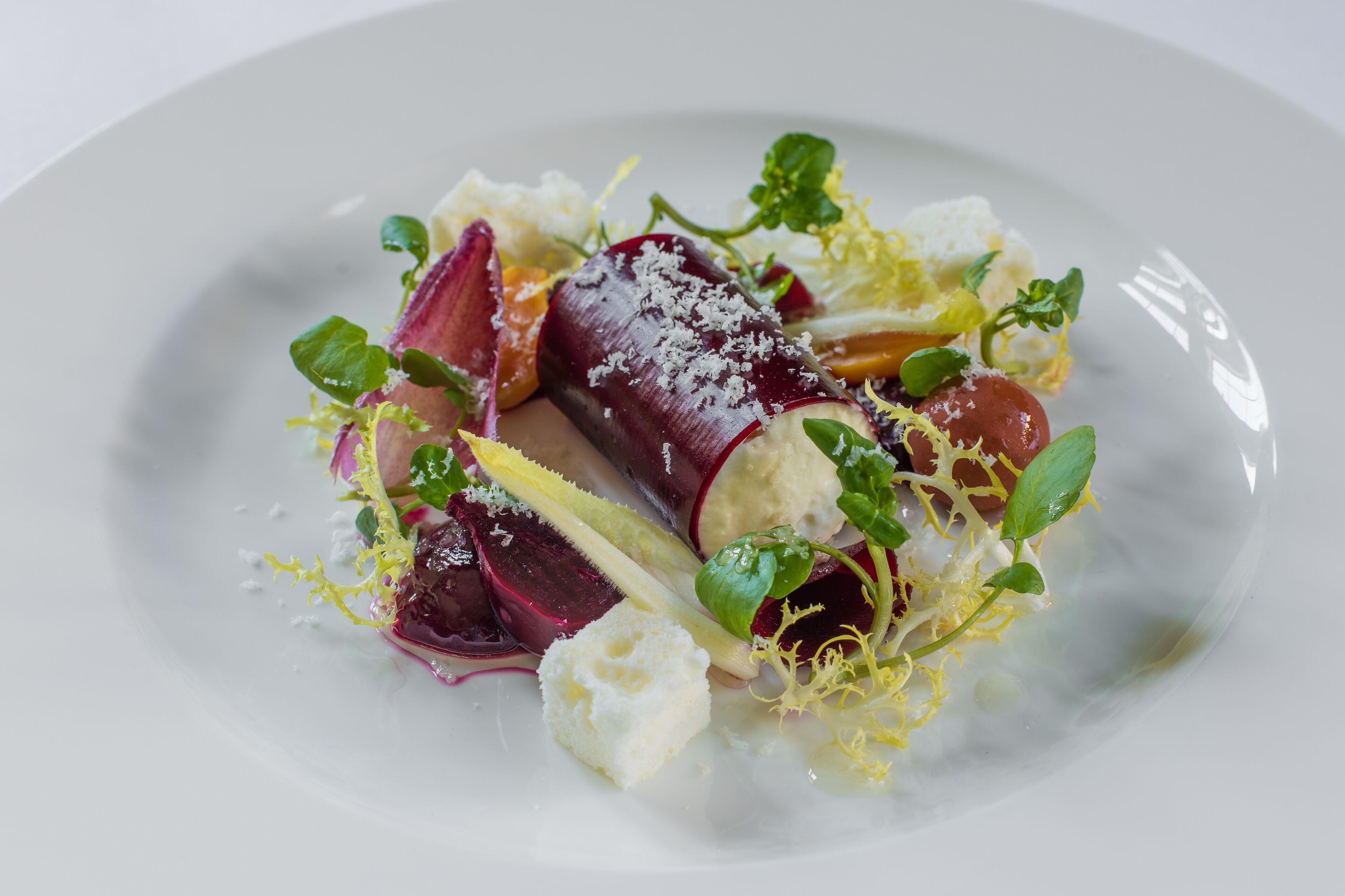 A white plate with a salad consisting of beets, cheese, and greens.