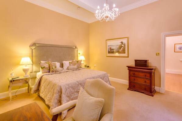 Un dormitorio con una cama grande, dos lámparas de noche, un candelabro, un aparador de madera y un cuadro enmarcado en la pared.