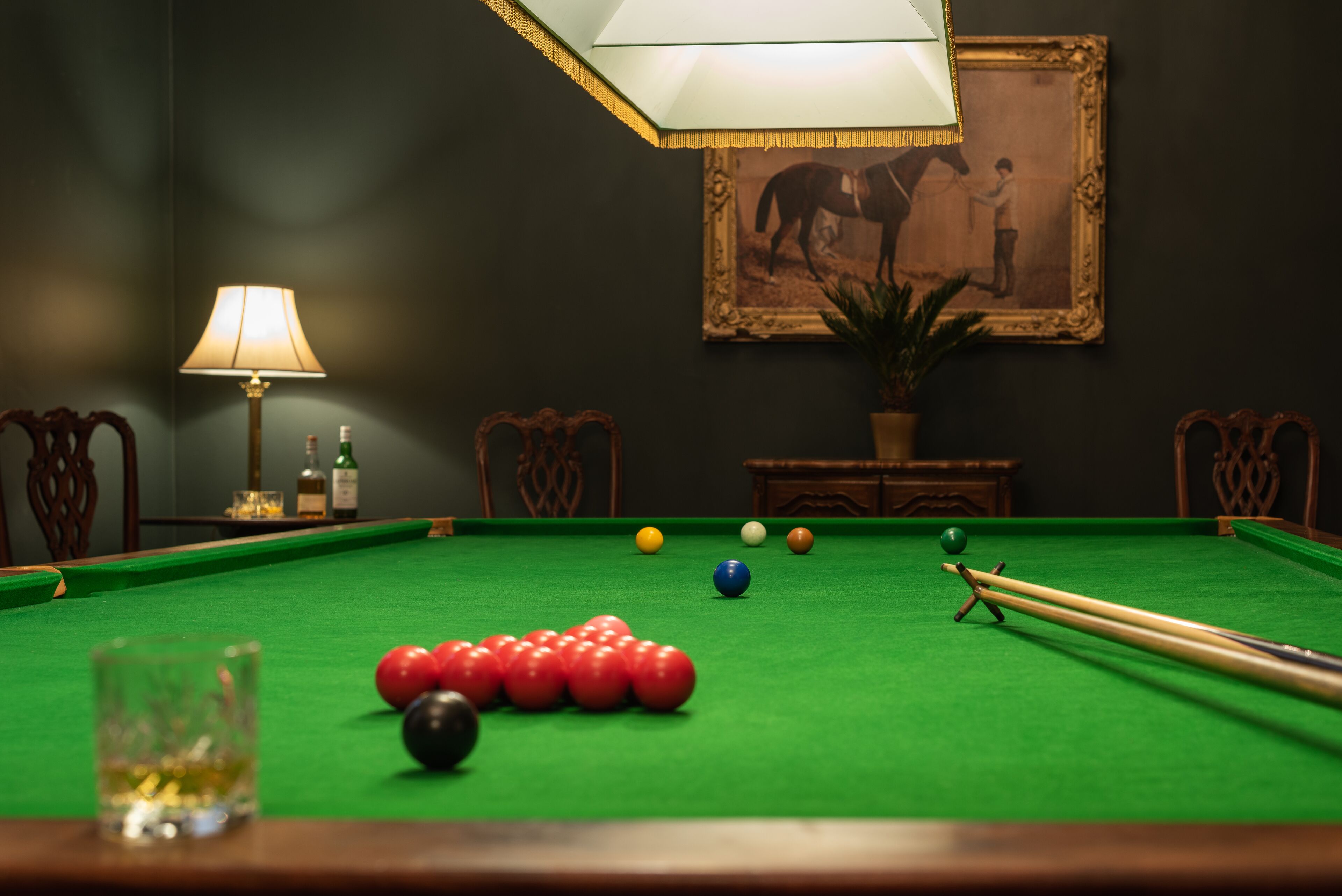 A pool table with balls, a lamp, and a framed picture on the wall.