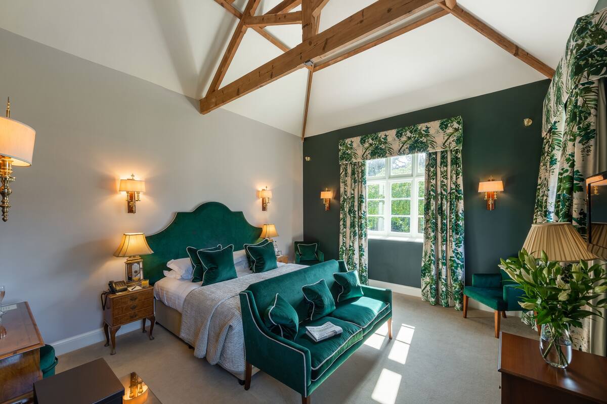 Une chambre à coucher avec un grand lit, des meubles recouverts d’un tissu vert et une fenêtre avec des rideaux.