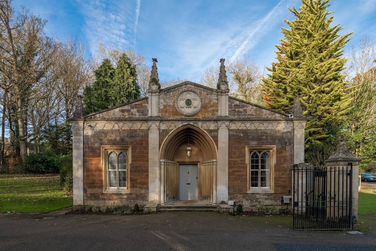 Un petit bâtiment en pierre avec une porte d’entrée en arc de cercle au centre, flanquée de deux fenêtres, et une horloge au-dessus de la porte.