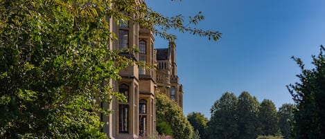A large, historic building with multiple windows and a well-maintained garden.