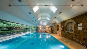 Una piscina interior con paredes de vidrio transparente, una pared de piedra en un lateral y un techo con tragaluces.
