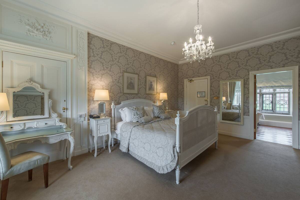 Une chambre à coucher avec un grand lit, une coiffeuse avec un miroir, un bureau et un lustre.