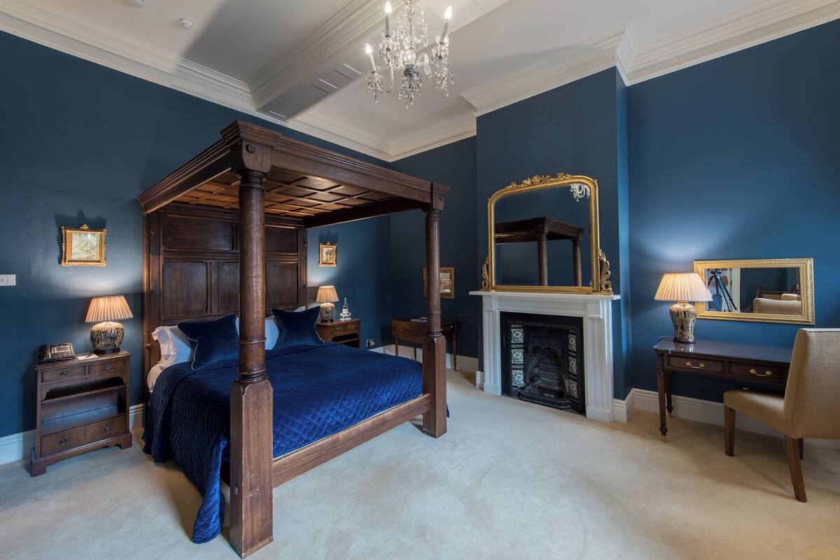 Un lit à baldaquin dans une pièce aux murs bleu foncé, avec une cheminée et un grand miroir.