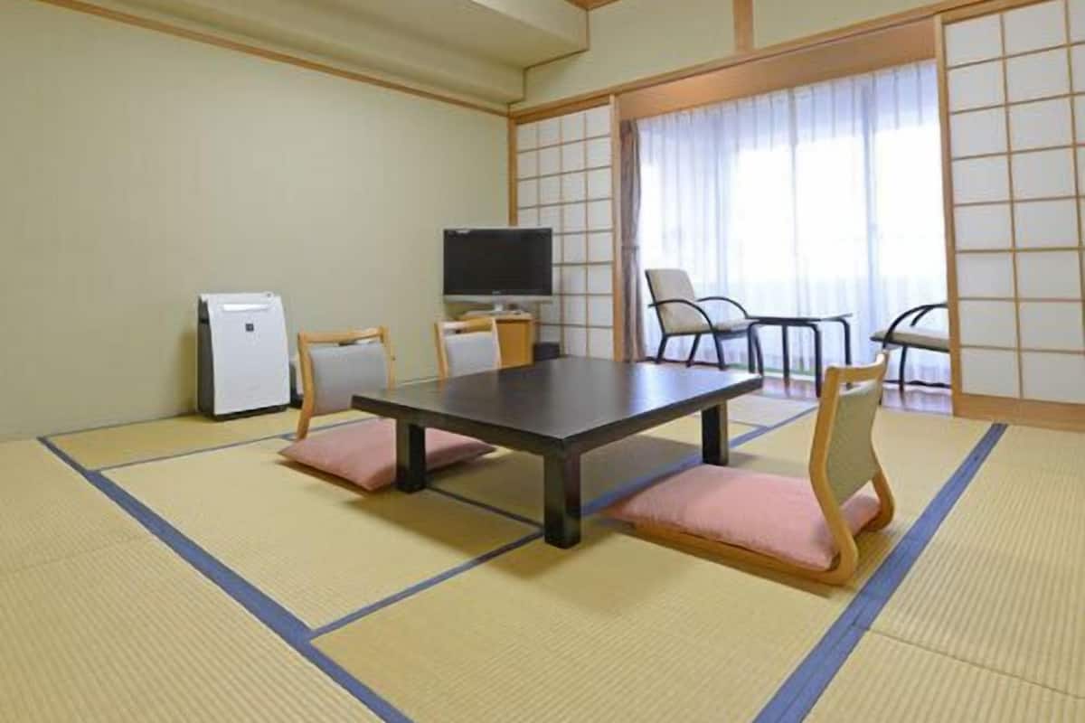 A tatami mat room with a table, chairs, a television, and a small refrigerator.
