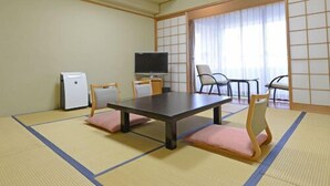 Une pièce avec un sol recouvert de tatamis, comprenant une table, des chaises, un téléviseur et un réfrigérateur.