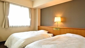 Une chambre d’hôtel avec deux lits, une fenêtre avec des rideaux, une lampe fixée au mur et une tête de lit en bois.