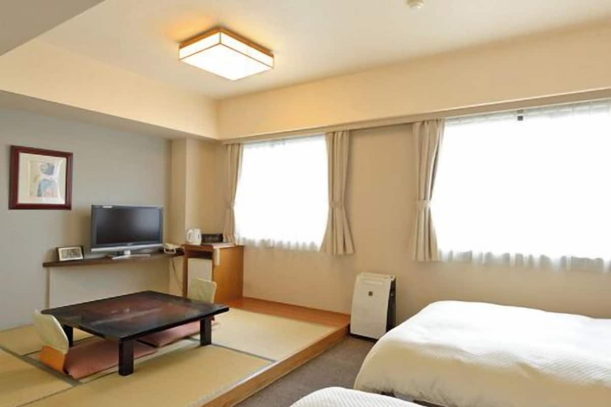 A hotel room with a bed, a desk, a television, and a window with curtains.