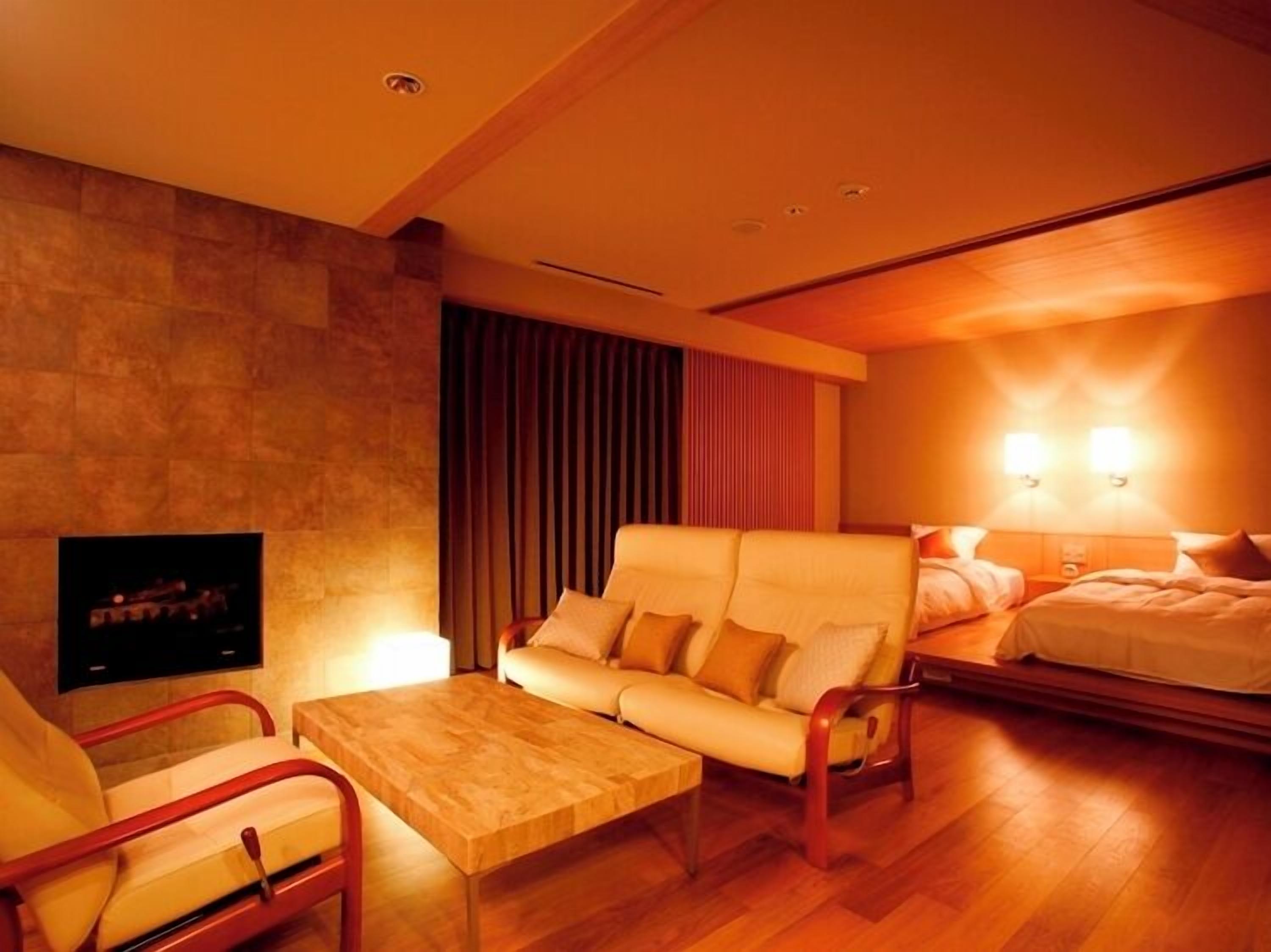A hotel room with a sofa, a coffee table, a TV, a bed, and a wall-mounted lamp.