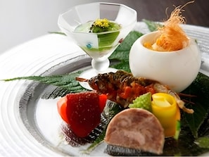 Un plato con diferentes alimentos, incluyendo un pescado, un tomate, algo amarillo y una verdura verde.