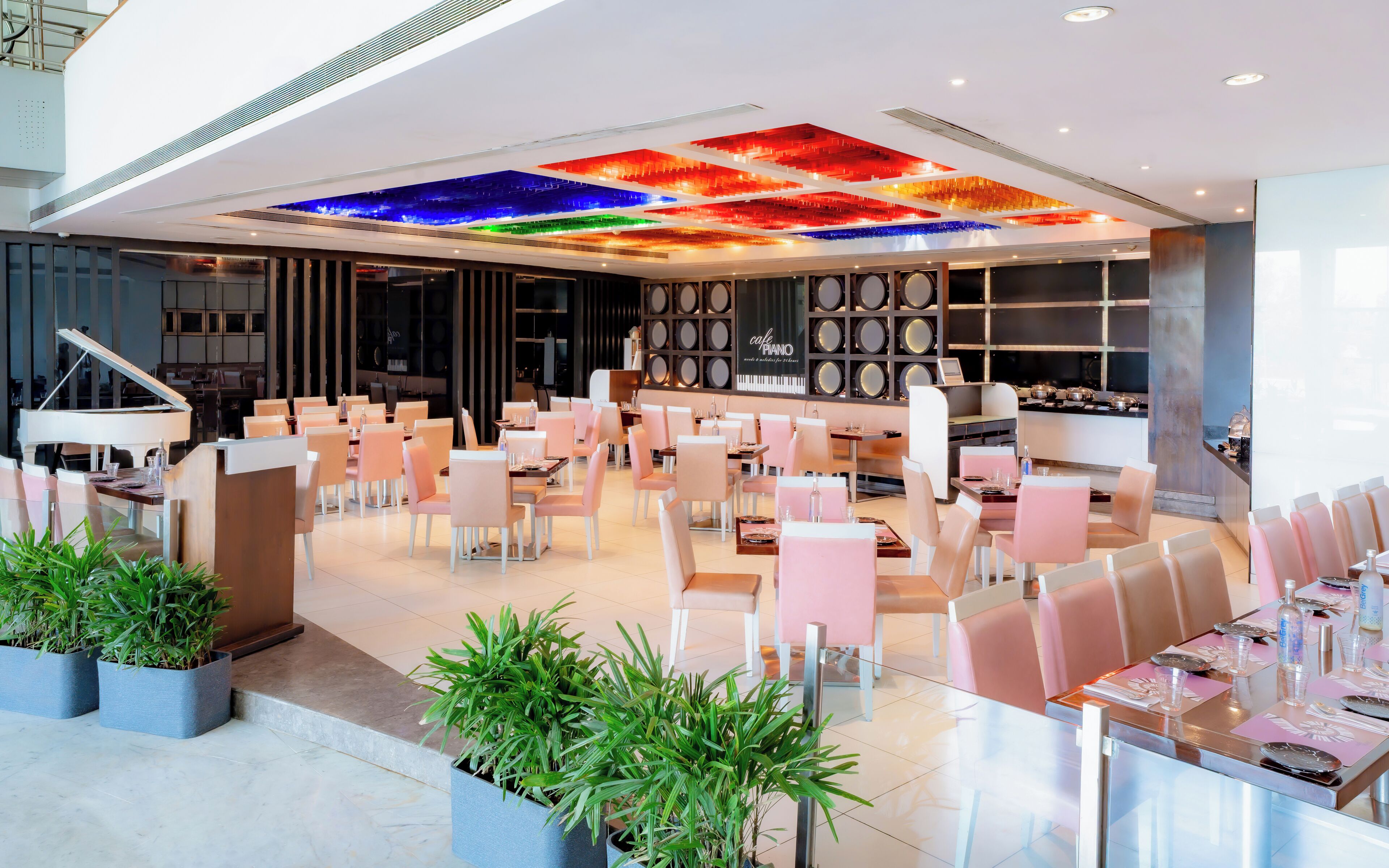 A modern restaurant with a piano, seating areas, and a ceiling with colorful lighting.
