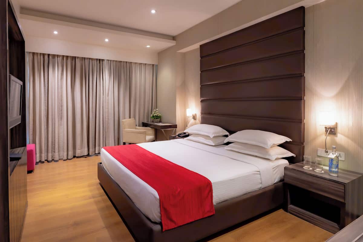 Une chambre d’hôtel avec un grand lit, un bureau avec une chaise, une télévision et une table de chevet avec une lampe.