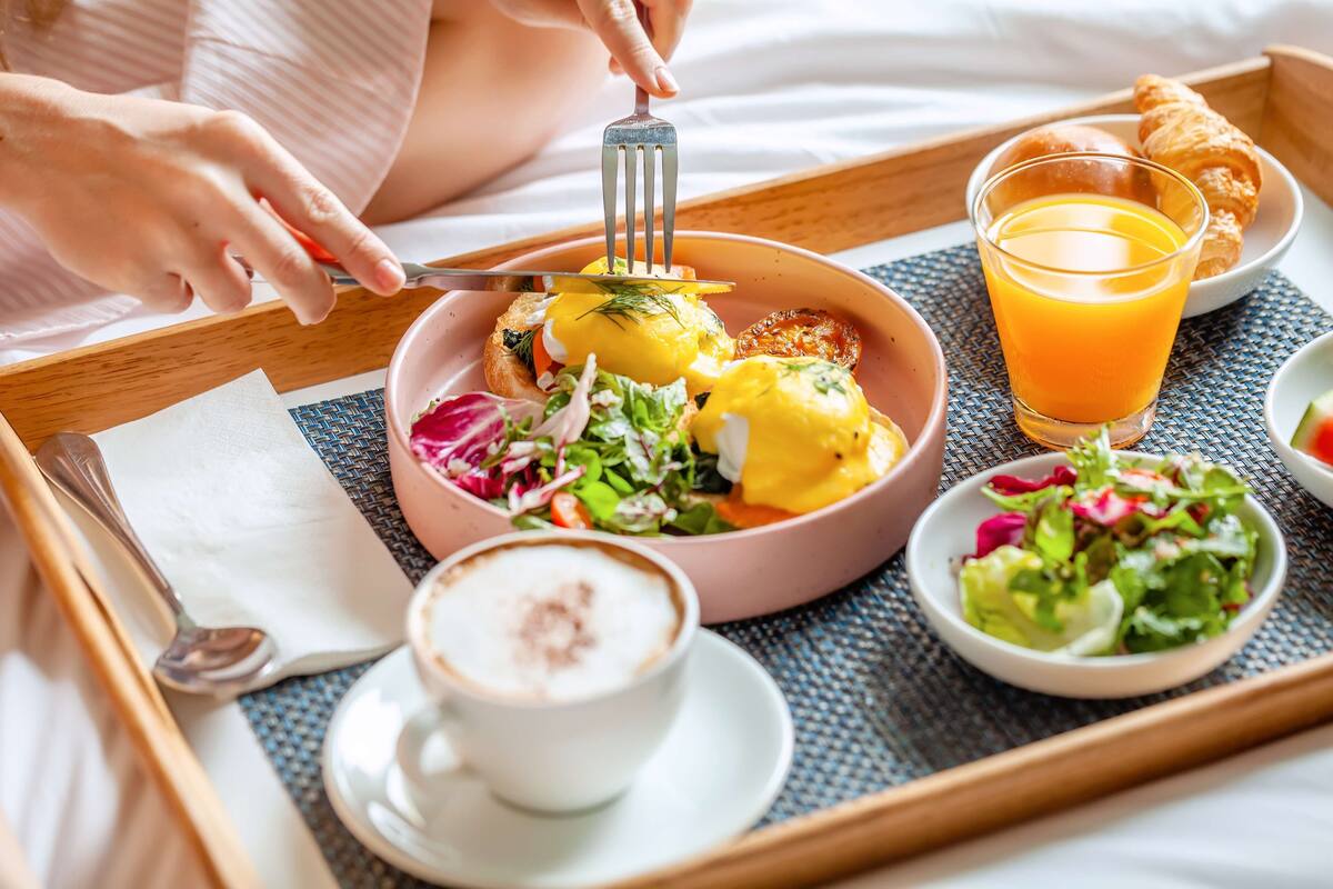 A breakfast tray with eggs benedict, a glass of orange juice, a croissant, and a cup of coffee.