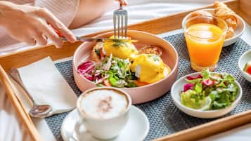 A breakfast tray with eggs benedict, a glass of orange juice, a croissant, and a cup of coffee.