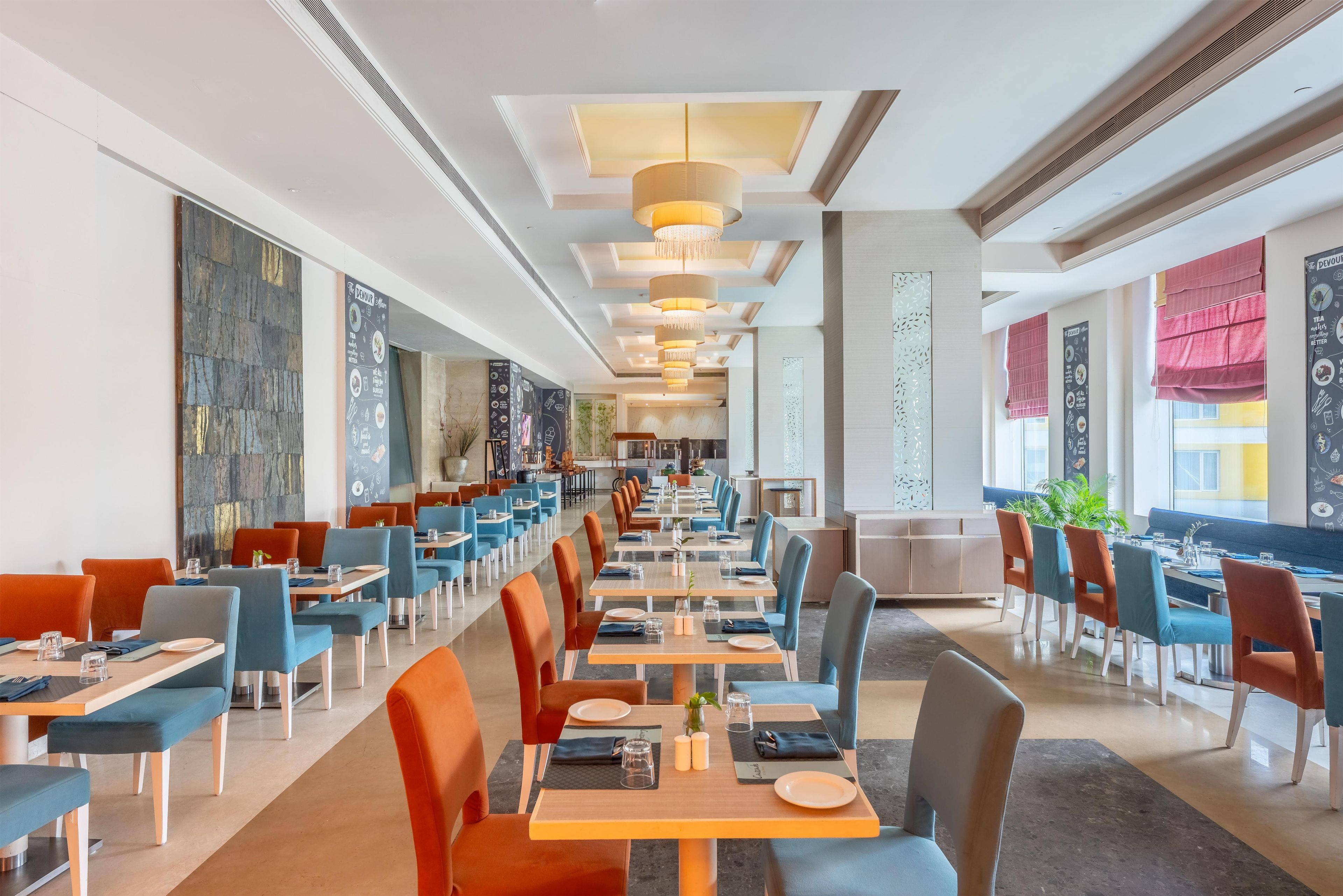 A spacious restaurant with long tables and chairs, a modern ceiling design, and large windows.