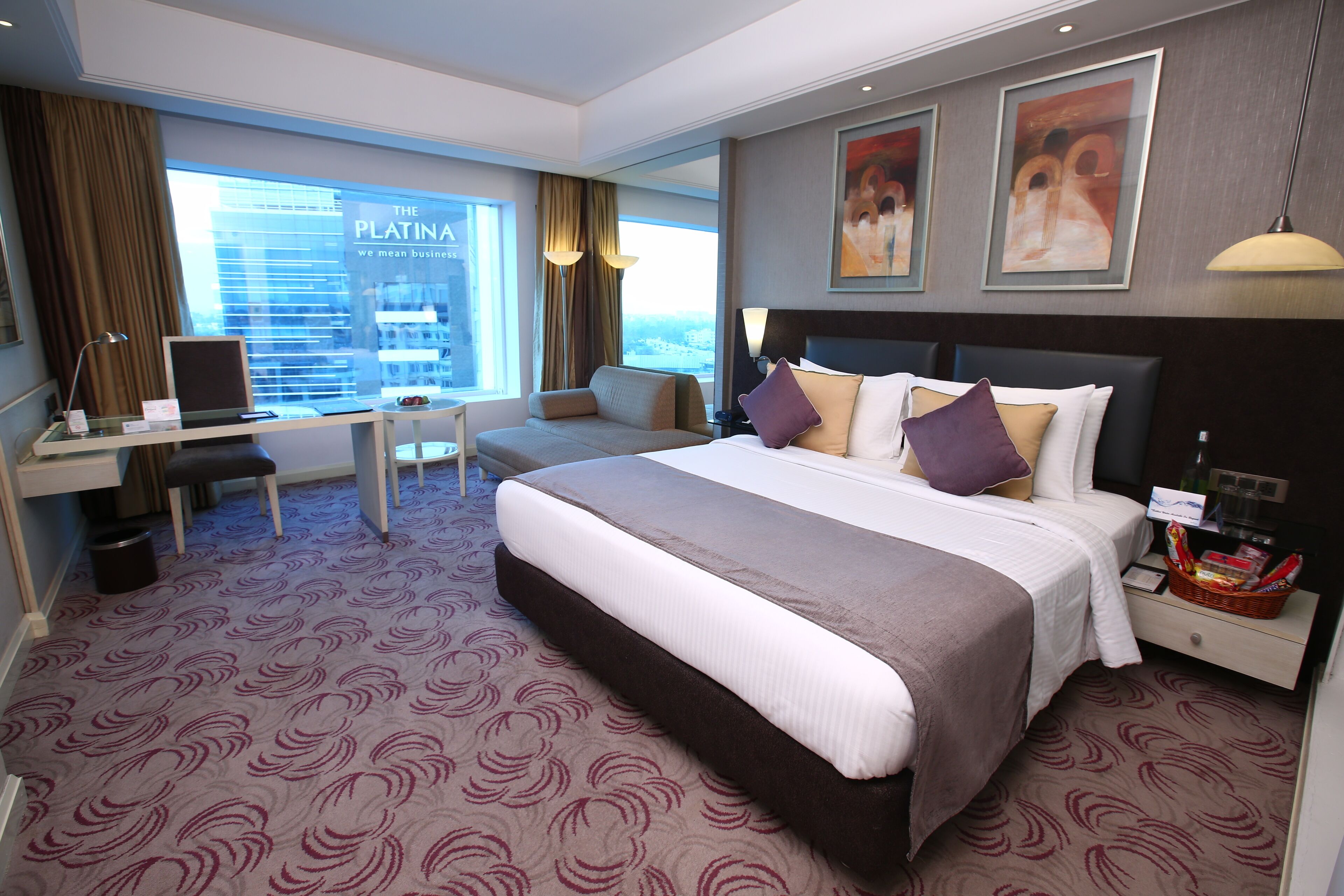 A hotel room with a large bed, a desk, a chair, and a view of a cityscape.