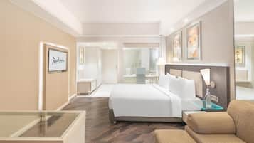 A hotel room with a bed, a glass table, a sofa, and a bathroom visible through an open door.
