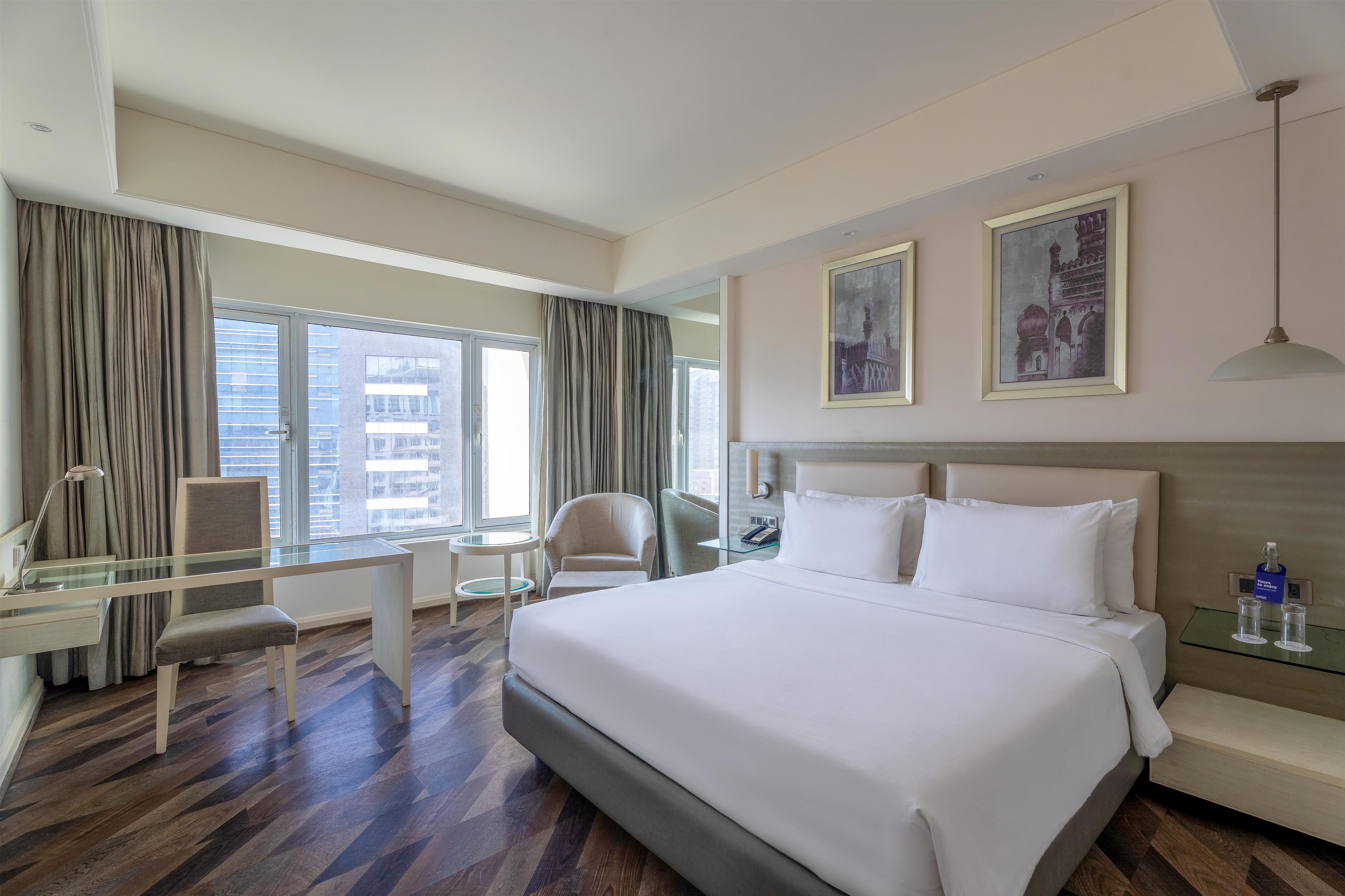 A hotel room with a bed, desk, chair, and large windows.