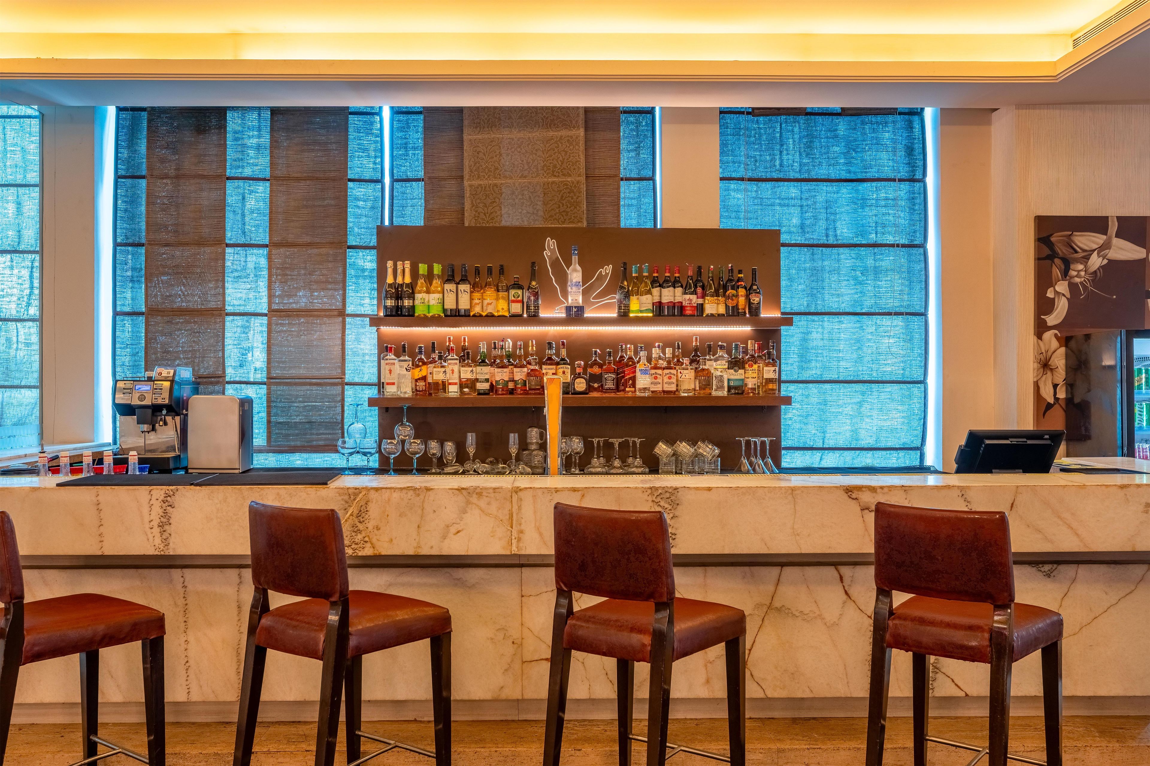 A bar area with a marble countertop, multiple shelves of liquor bottles, and three bar stools.