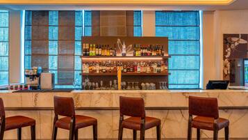 A bar area with a marble countertop, multiple shelves of liquor bottles, and three bar stools.