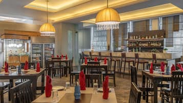 Un restaurante con varias mesas, servilletas rojas y una zona de bar con botellas.