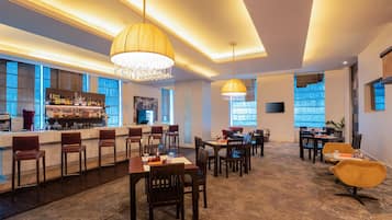 Eine moderne Bar mit einer langen Theke, mehreren Barhocker und einer Auswahl an Flaschen. Es gibt Esstische mit Stühlen, die für Gäste bereitstehen.